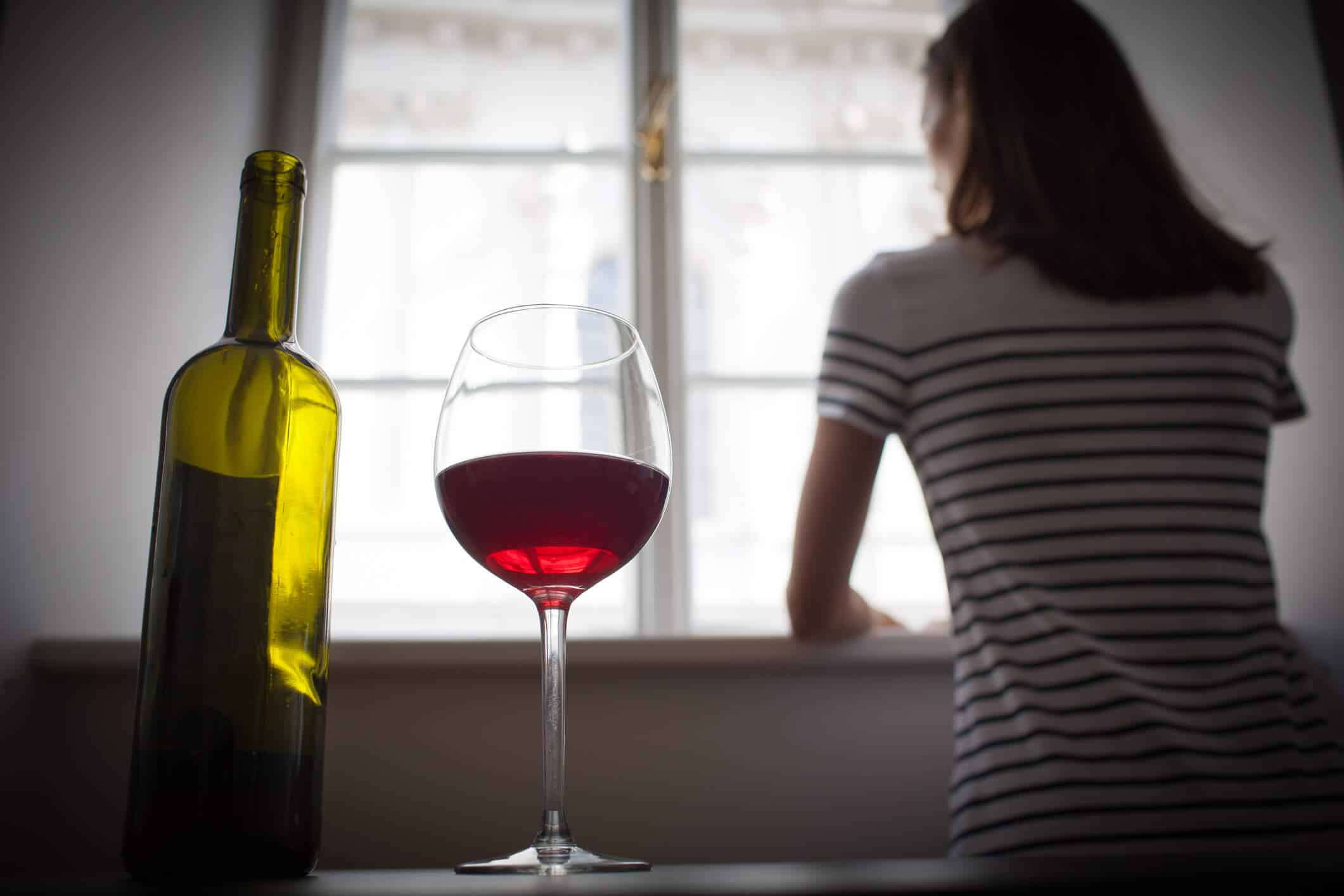 Bouteille et verre de vin avec une femme qui regarde par la fenêtre