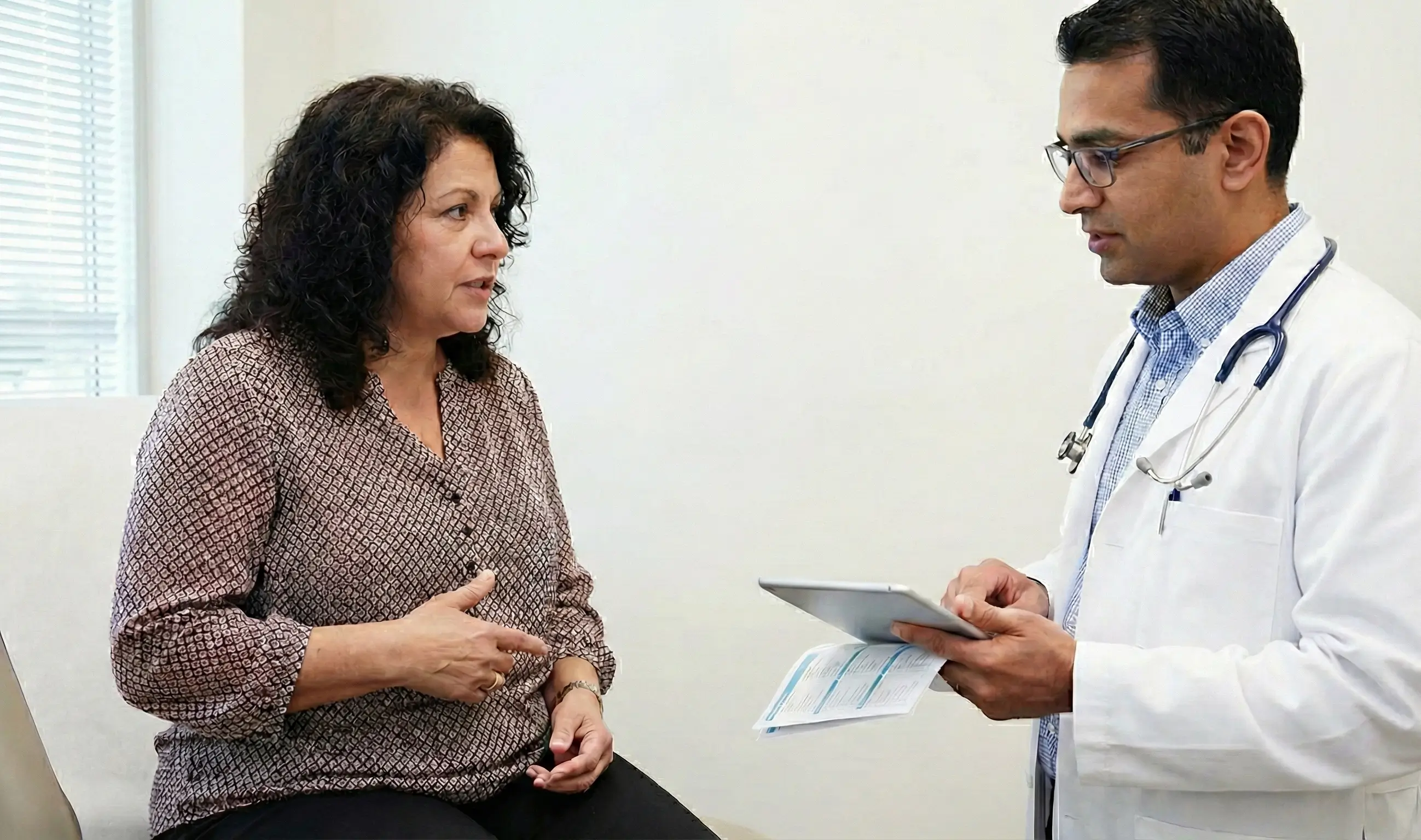 Une femme échange avec son médecin sur sa santé abdominale lors d'une consultation médicale dans un cabinet sobre et professionnel.