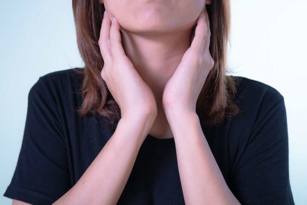 Femme se touchant la gorge, douleur évocatrice d'une angine chez l'adulte